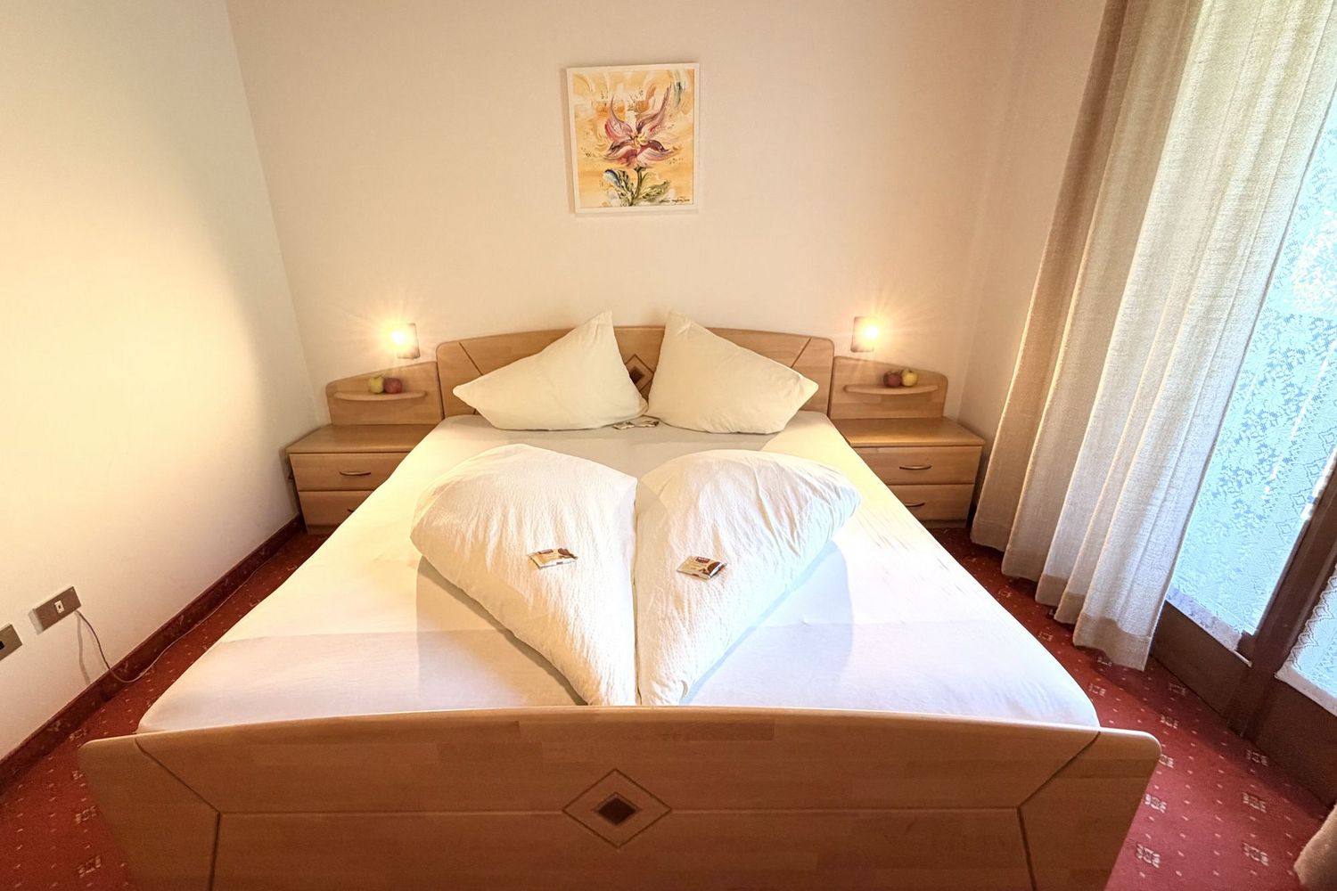 Double bed with light wooden furniture, heart-shaped pillows, and atmospheric lighting in a cozy hotel room.