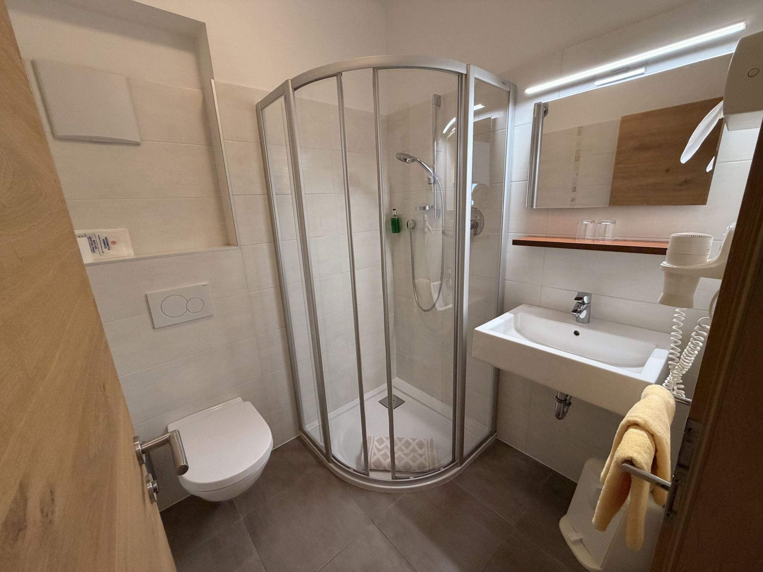 A modern, brightly tiled bathroom with a quadrant glass shower cabin, a wall-mounted toilet, and a sink with a mirror above.