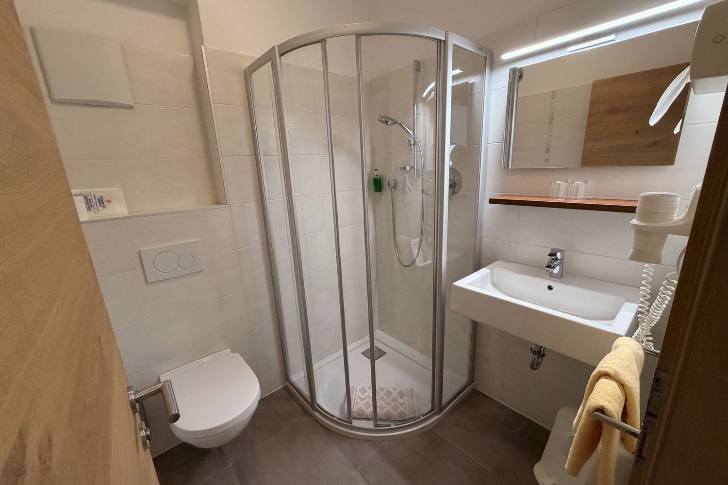 A modern, brightly tiled bathroom with a quadrant glass shower cabin, a wall-mounted toilet, and a sink with a mirror above.
