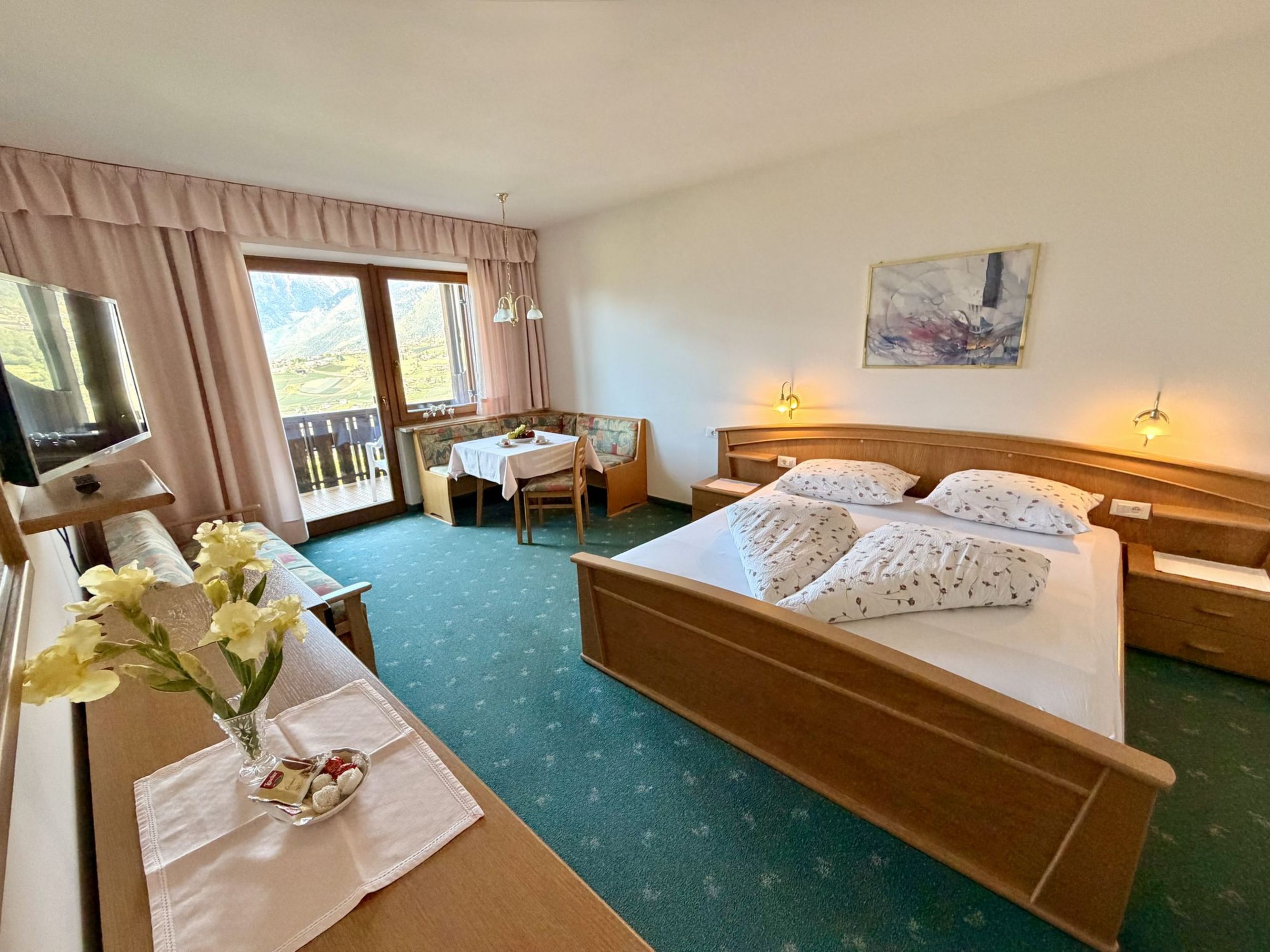 Ein gemütliches Hotelzimmer im alpenländischen Stil mit Doppelbett, Sitzecke am Fenster mit Bergblick und einem Flachbildfernseher.