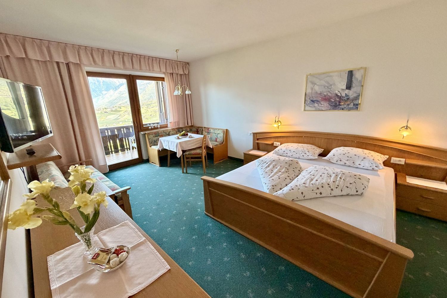 Ein gemütliches Hotelzimmer im alpenländischen Stil mit Doppelbett, Sitzecke am Fenster mit Bergblick und einem Flachbildfernseher.