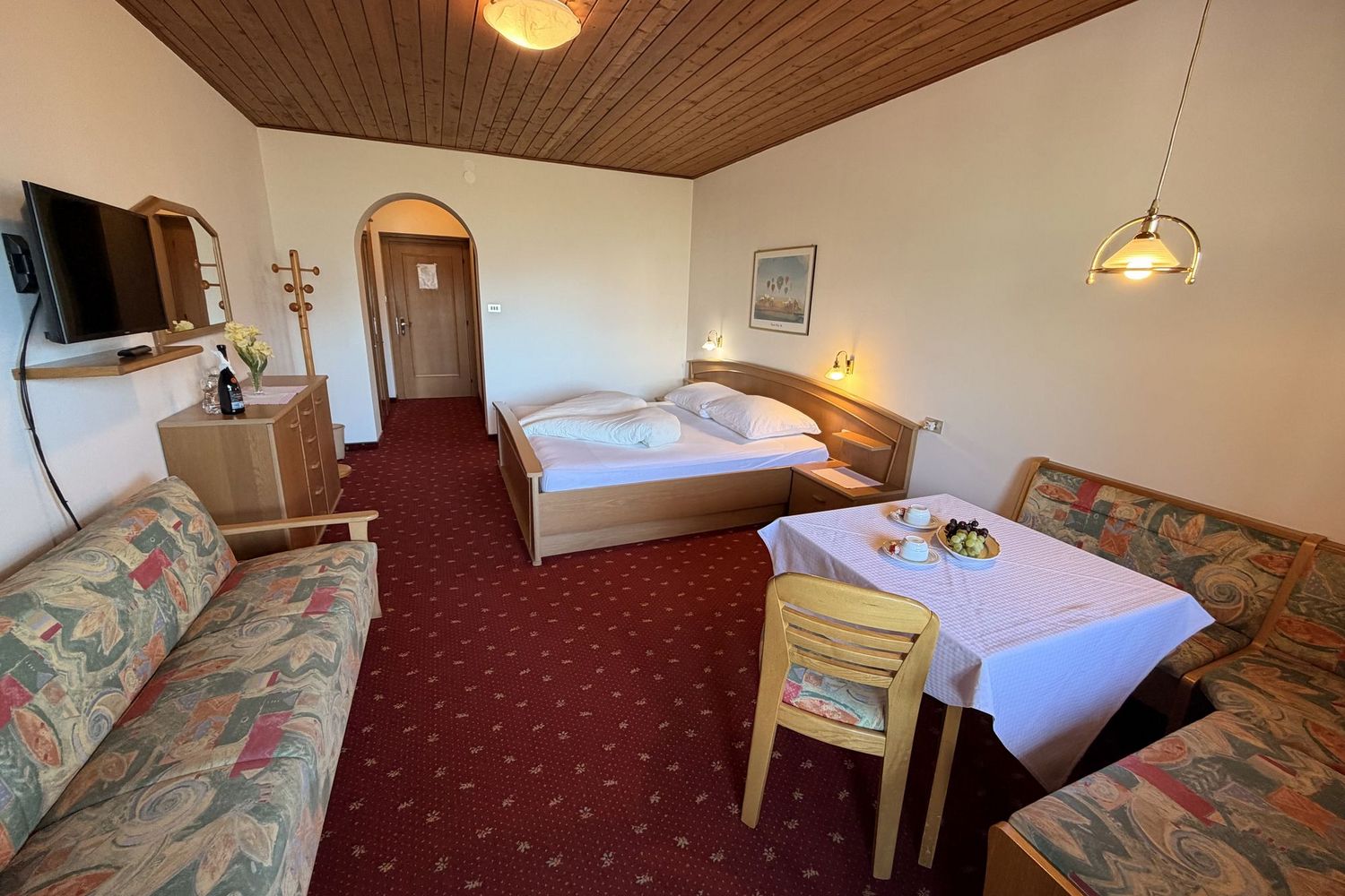 Ein Hotelzimmer mit Doppelbett, Sitzecke mit Tisch, roten Teppichboden und einer Holzdecke.