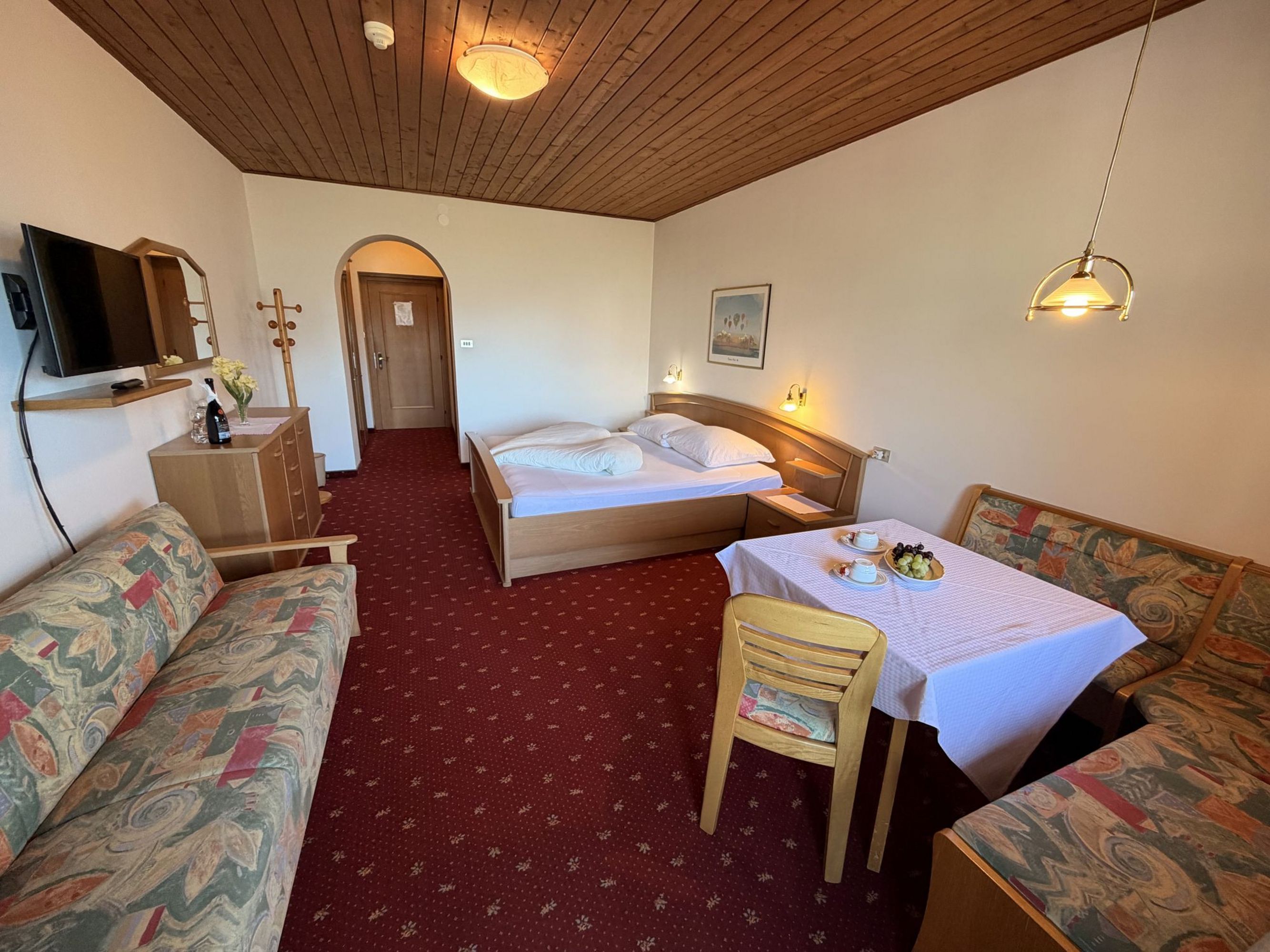 Ein Hotelzimmer mit Doppelbett, Sitzecke mit Tisch, roten Teppichboden und einer Holzdecke.